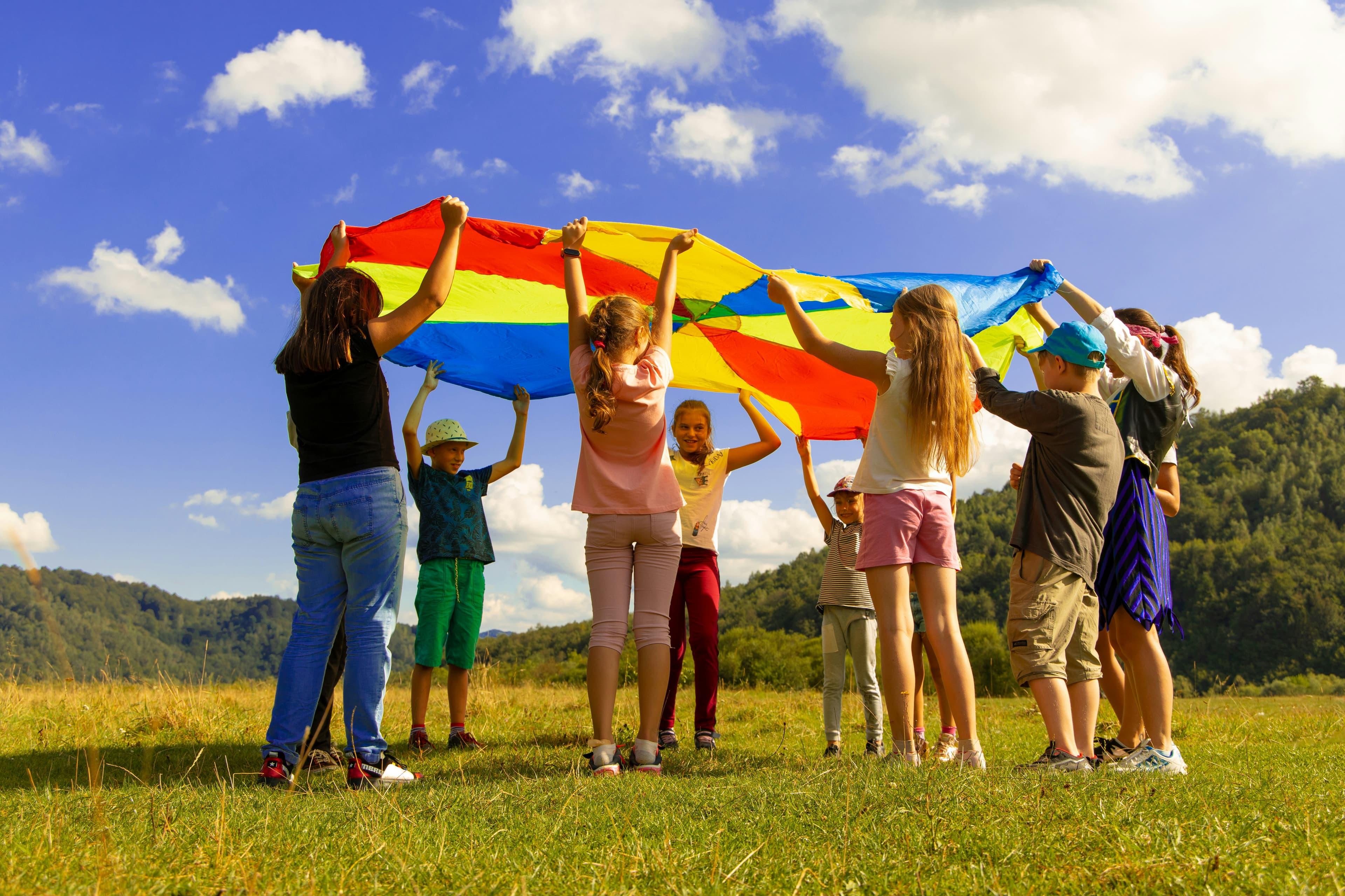 Children Playing with a Multi-Colored Parachute in Green Grass with a blue sky in the background